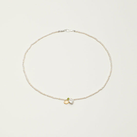 A delicate silver chain necklace with a small double-heart charm in gold and silver, displayed on a clean, light beige background.