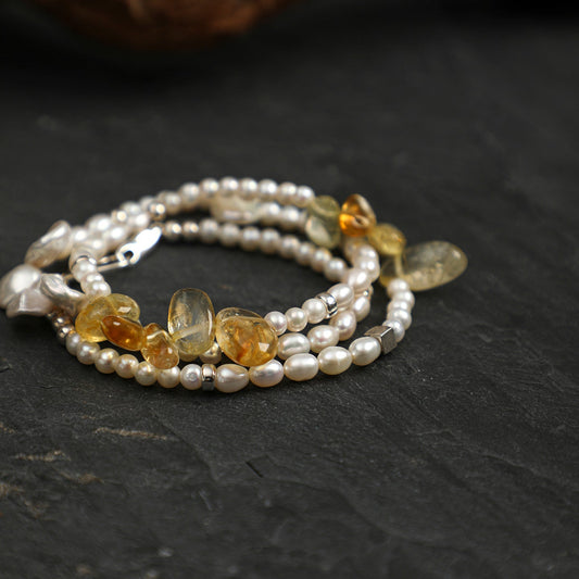 A multi-strand beaded bracelet featuring white freshwater pearls and polished amber-colored beads, displayed on a dark slate surface.