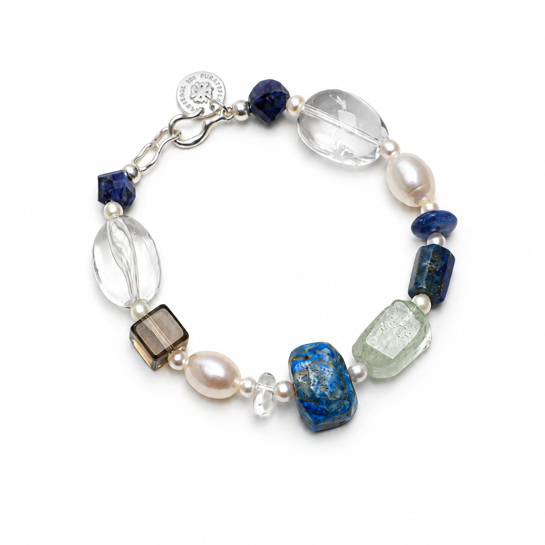 A beaded bracelet featuring a mix of blue, clear, white, and smoky brown gemstone beads, accented by white pearls and a silver-tone clasp with a round charm.