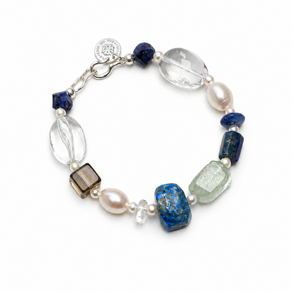 A beaded bracelet featuring a mix of blue, clear, white, and smoky brown gemstone beads, accented by white pearls and a silver-tone clasp with a round charm.