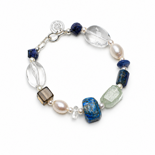 A beaded bracelet featuring a mix of blue, clear, white, and smoky brown gemstone beads, accented by white pearls and a silver-tone clasp with a round charm.
