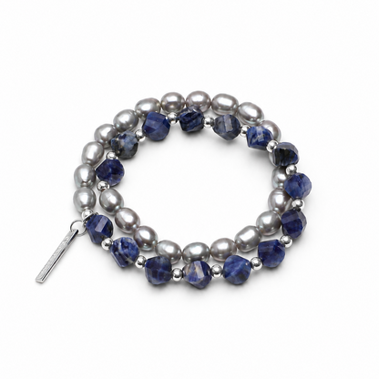 A double-strand beaded stretch bracelet featuring dark blue faceted beads and silver-gray baroque pearls, accented with small silver spacer beads and a silver toggle clasp, shown on a light cream background.